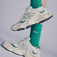 White sneakers with green accents worn with green socks on a light gray background
